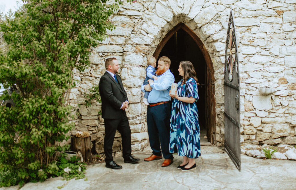 Freier Redner Tom Salzlechner mit einer kleinen Familie mit Kind vor einer Kapelle aus Stein