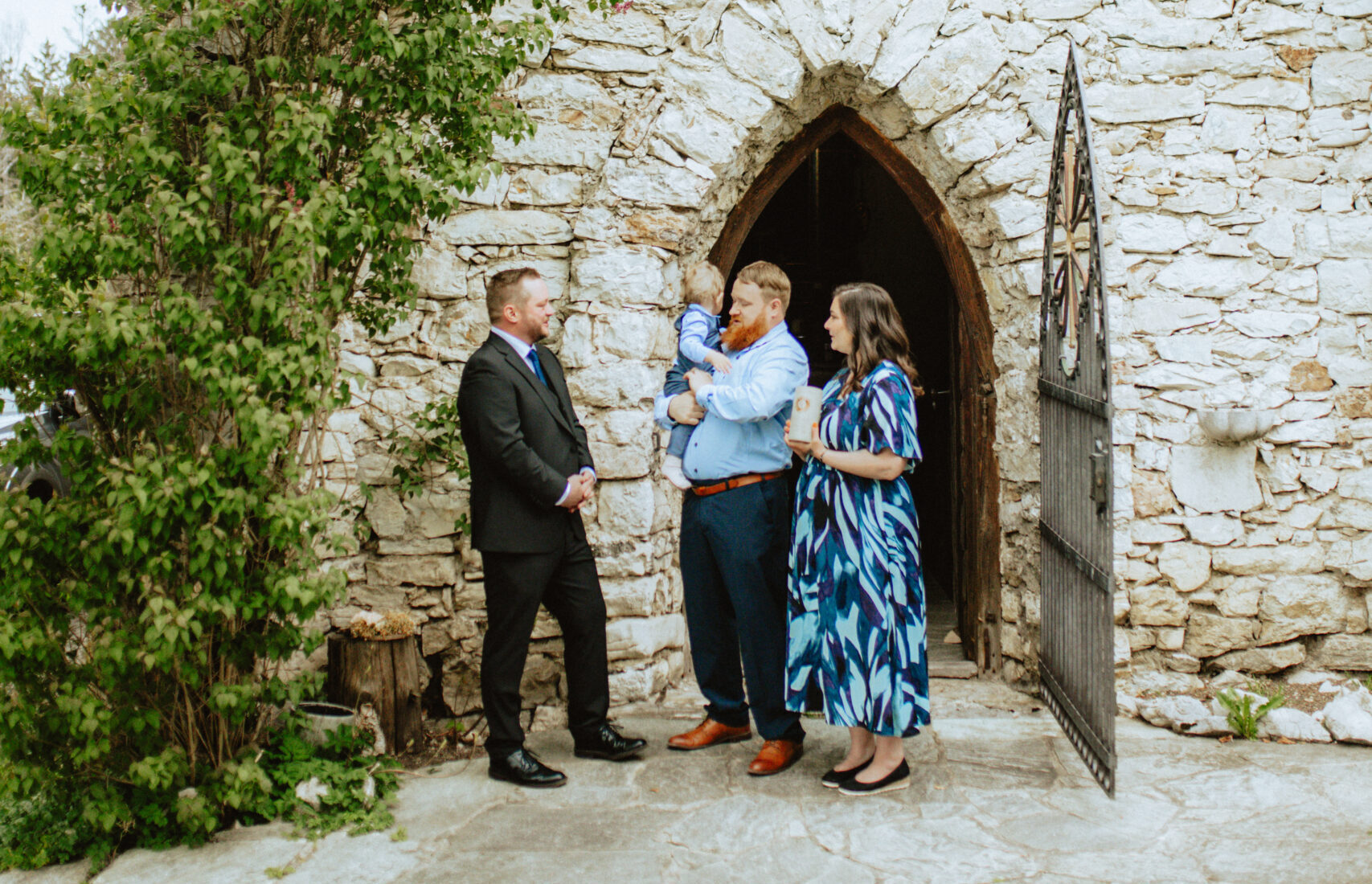 Freier Redner Tom Salzlechner mit einer kleinen Familie mit Kind vor einer Kapelle aus Stein