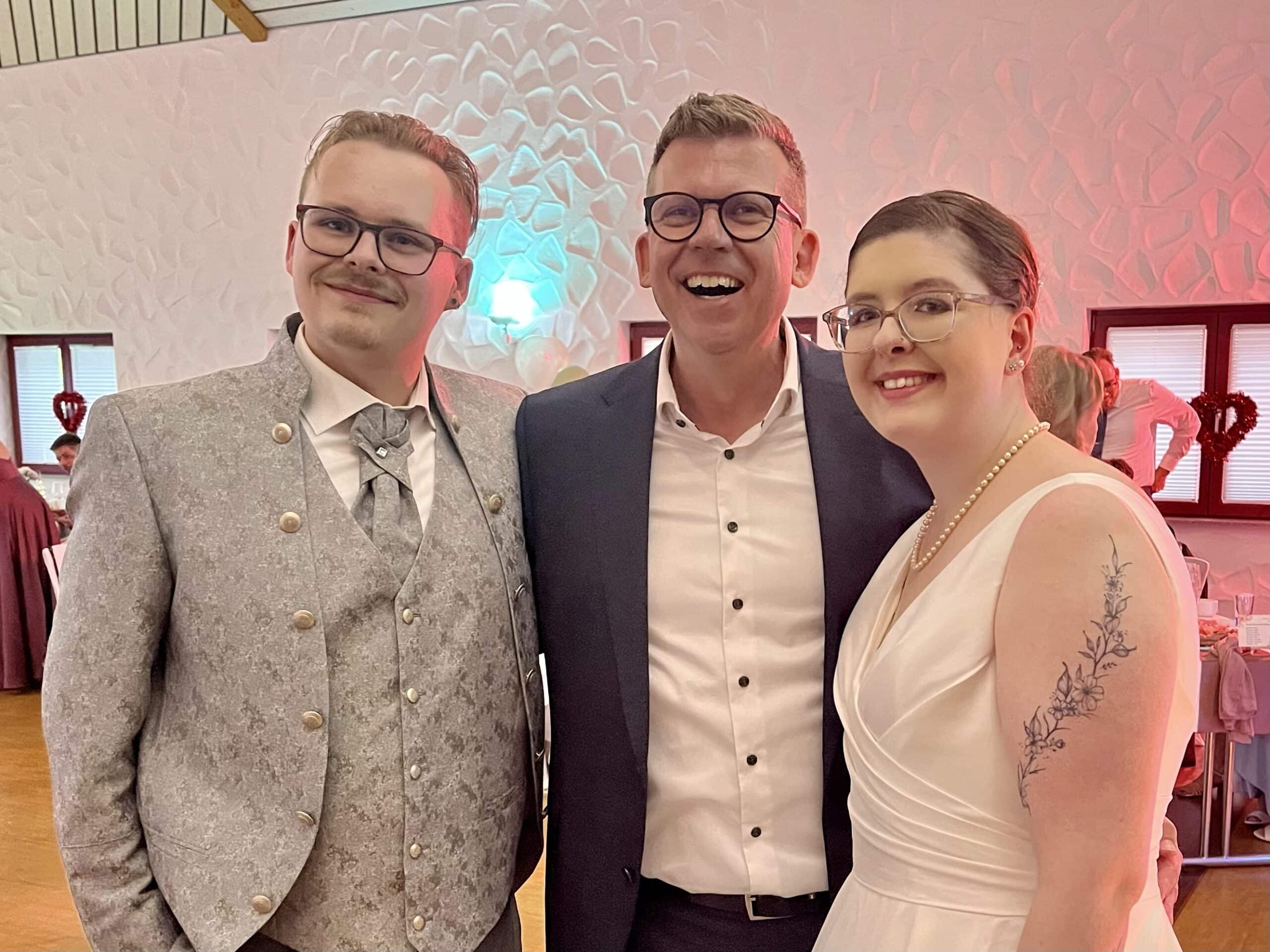 Trauredner Andreas Luck strahlt mit seinem Hochzeitspaar in die Kamera