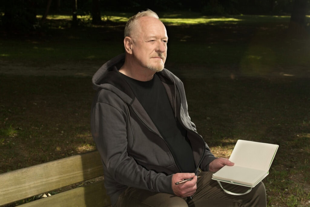 Jens Cording sitzt auf einer Parkbank mit einem Laptop, bereit für eine Rede oder Präsentation im Freien. Perfekt für professionelle Redner, die flexible Veranstaltungsorte suchen.