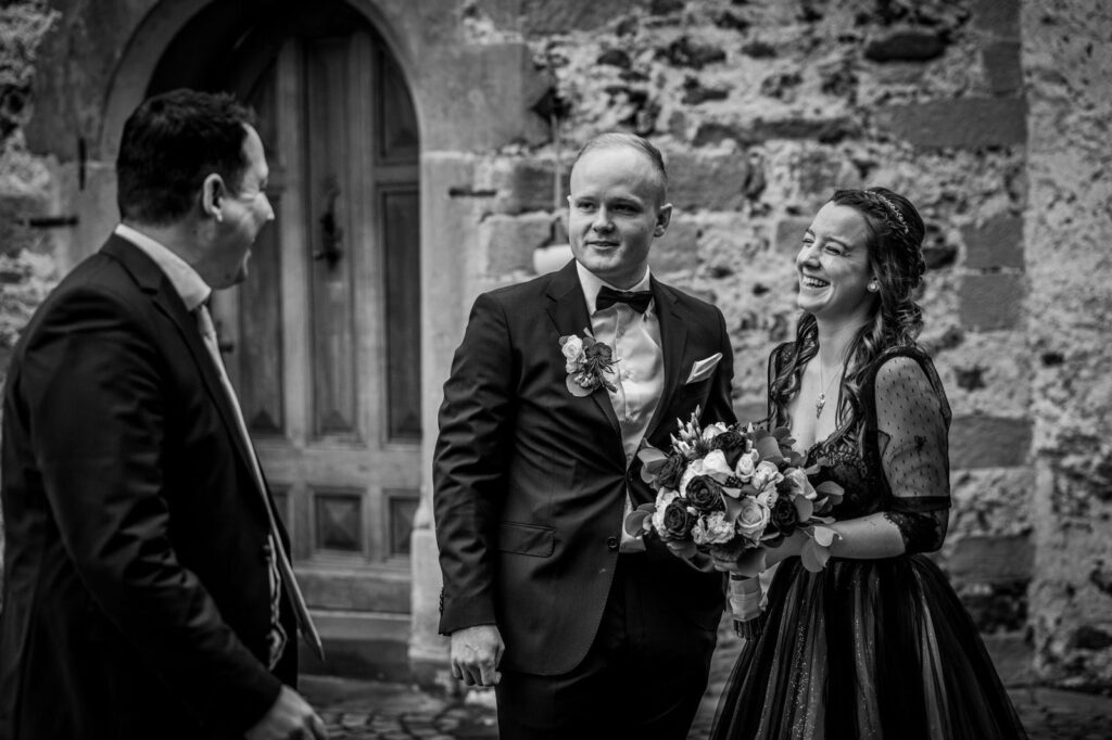 Hochzeitspaar mit Redner bei der Zeremonie, lachend und glücklich, in historischem Ambiente, Hochzeitsfeier, professionelle Traurede, Freie Redner, emotionale Zeremonie.