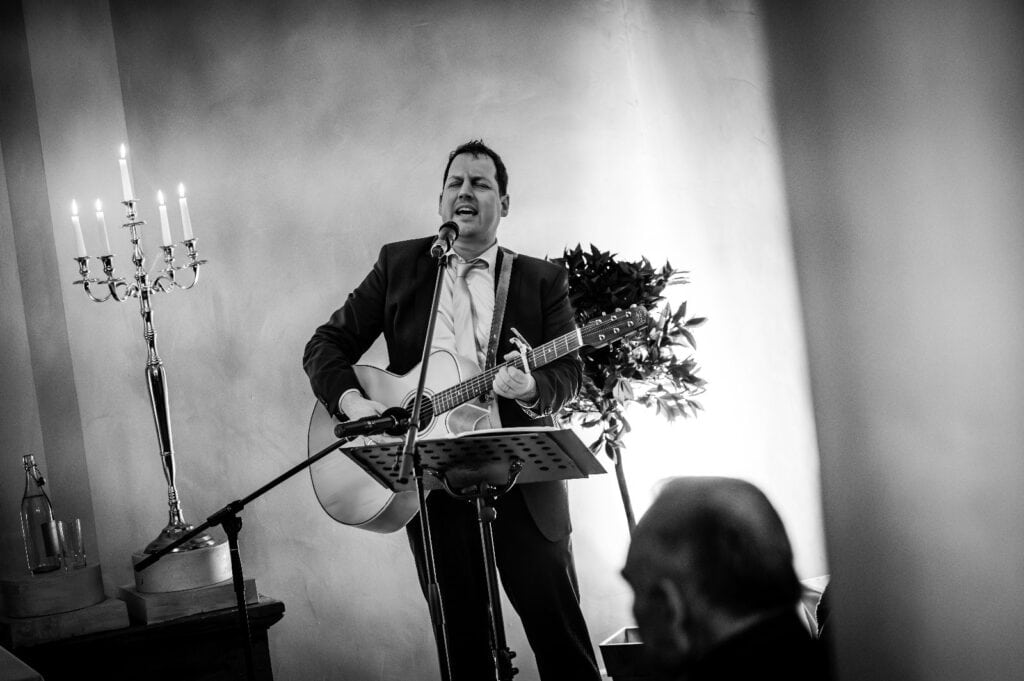 Musiker bei einer freien Rede mit Gitarre, singend vor Publikum in einem stilvollen Raum. Perfekt für Hochzeiten, Trauungen und Events.