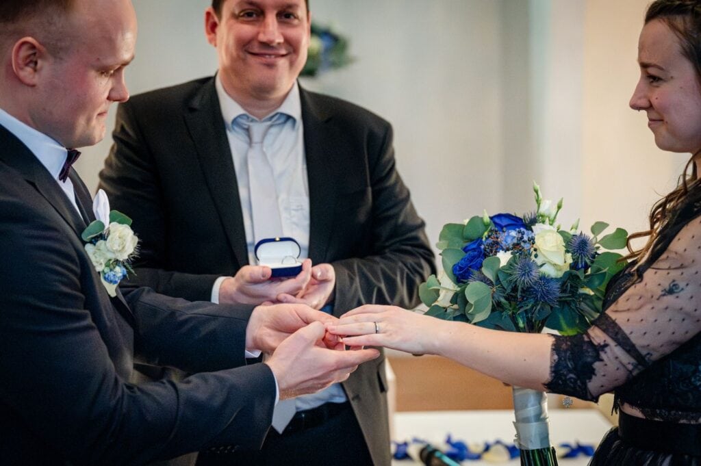 Hochzeitspaar bei der Trauung mit freiem Redner, der den Moment mit einem Ringwechsel begleitet, umgeben von Freunden und Familie.