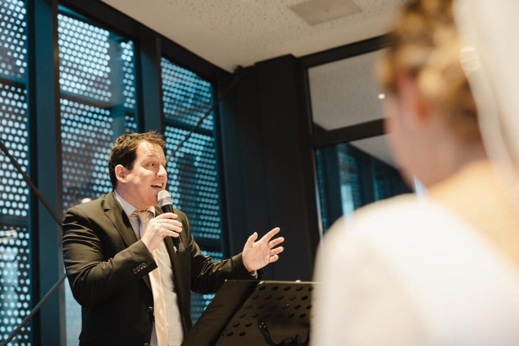 Ein freier Redner hält eine inspirierende Rede bei einer Veranstaltung, während das Publikum aufmerksam zuhört. Perfekt für Hochzeiten, Firmenveranstaltungen und private Feiern.