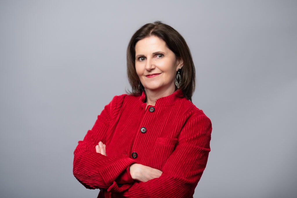 Selbstbewusste Frau in rotem Blazer, die professionell und freundlich wirkt, ideal für Redner- und Präsentationsaufnahmen.