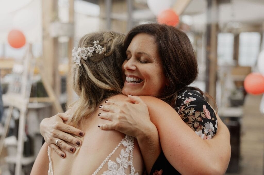 Zwei Frauen umarmen sich herzlich bei einer freien Trauung, symbolisiert Liebe und Verbundenheit, in einem festlichen Rahmen mit Dekorationen im Hintergrund.
