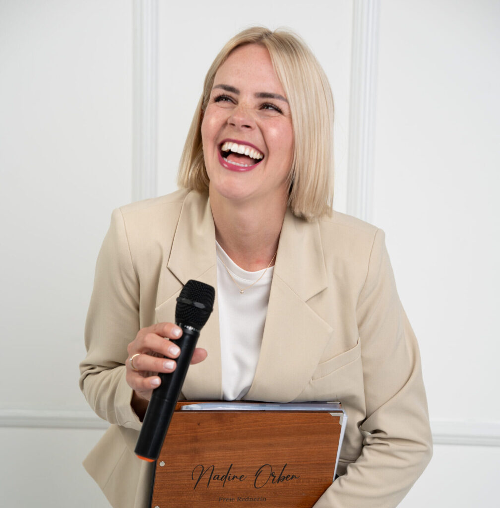 Hier sieht man unsere Freie Rednerin Nadine Orben mit ihrer Rednermappe und einem Mikrofon in die Kamera lachen