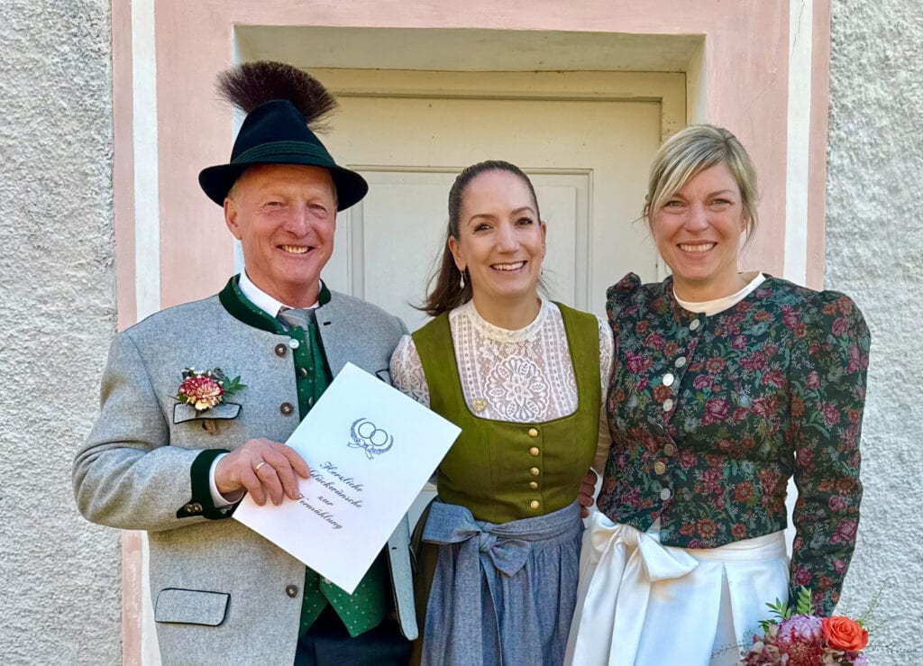 Hochzeitspaar mit Rednerin bei einer Zeremonie im Freien, lachend und in traditioneller Kleidung, symbolisiert eine persönliche Trauung im Freien.