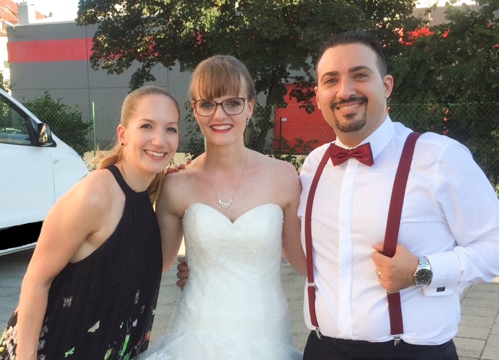 Fröhliches Hochzeitspaar mit Redner bei einer Feier im Freien, lachend und glücklich, in festlicher Kleidung, mit einem Redner, der eine wichtige Rolle bei der Veranstaltung spielt.