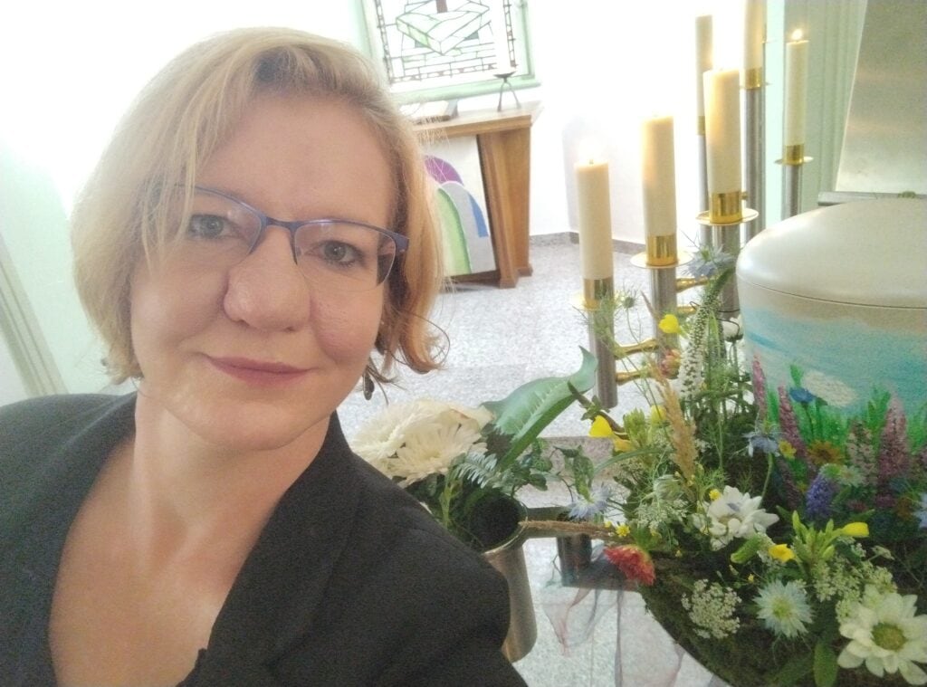 Frau mit Brille bei einer Trauerfeier, umgeben von Kerzen und Blumen, professionelle Rednerin bei einer Gedenkveranstaltung.