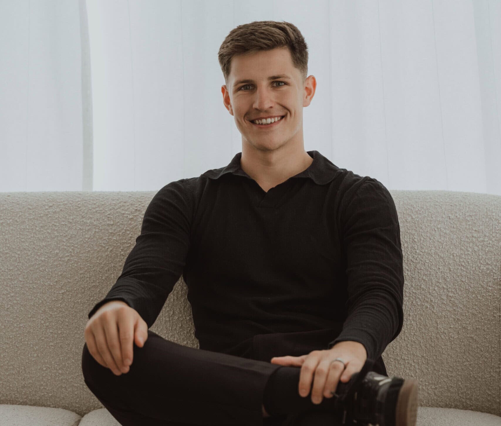 Junger freier Redner sitzt entspannt auf einem Sofa, lächelt freundlich und wirkt professionell für öffentliche Reden und Präsentationen.