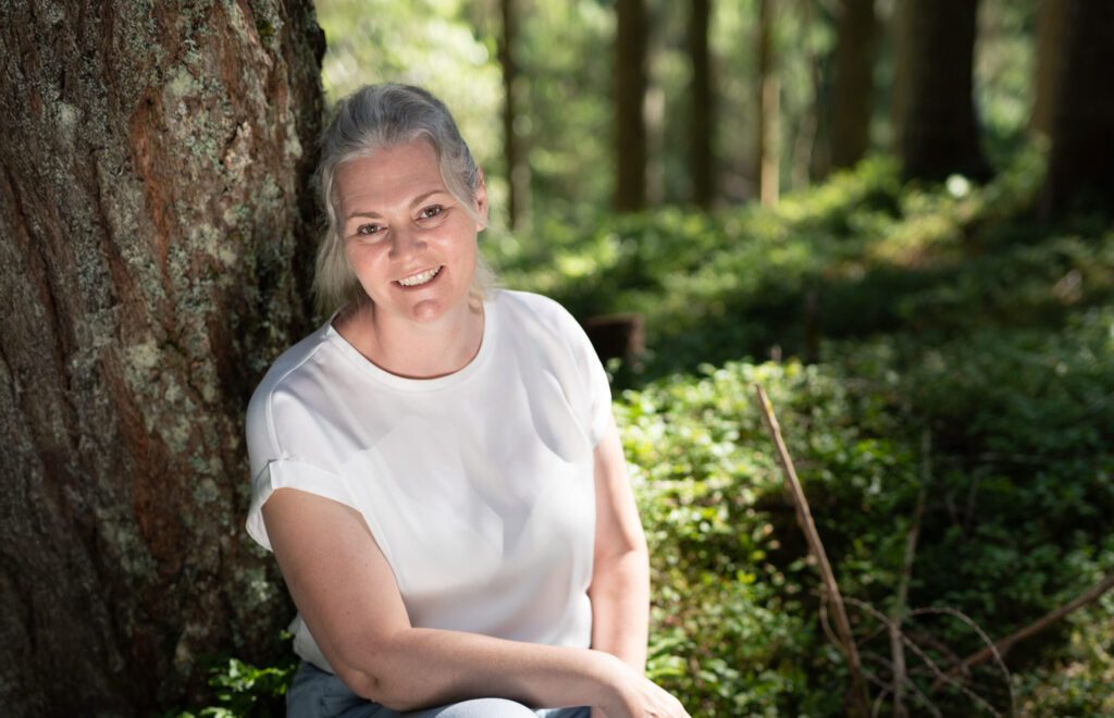 Freie Rednerin Ninja Habietinek sitzt im Wald an einen Baum gelehnt und blickt Richtung Kamera