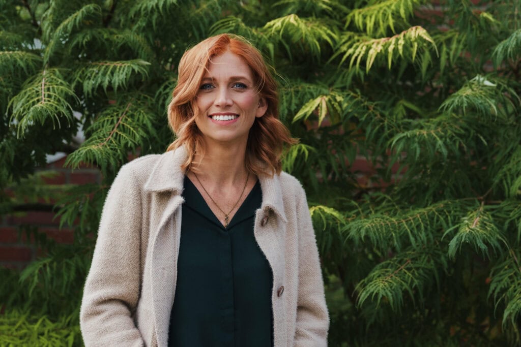 Freie Redner Frau mit roten Haaren vor grüner Natur, professionell und freundlich, ideal für Redner- und Eventthemen.